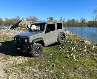Vista frontale di un noleggio Suzuki Jimny all'aeroporto di Podgorica, Montenegro ✓ Auto #15693. ✓ Cambio Automatico TM ✓ 0 recensioni.